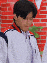 a young man wearing a white jacket with a red and blue collar is standing in front of a red brick wall