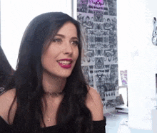 a woman with long dark hair is smiling in front of a wall with posters on it