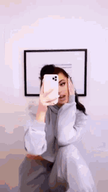 a woman is taking a selfie with her cell phone in front of a mirror .