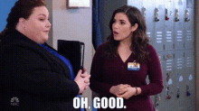 two women are standing next to each other in front of lockers and one of them is talking to the other .