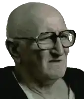 a bald man wearing glasses and a black shirt looks at the camera