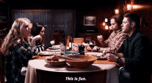a group of people are sitting around a table eating food and drinking wine and one of them says " this is fun "