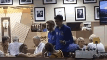 a group of people are sitting at a table in a restaurant with a man wearing a blue jacket with the number 18 on it