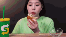 a woman is eating a subway sandwich next to a cup with the letter s on it