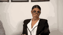 a woman wearing glasses and a suit is holding a pen and a clipboard .