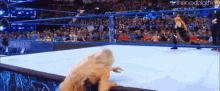 a woman is laying on the ground in a wrestling ring while a man stands behind her .