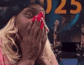 a woman with red nails is covering her face with her hands in front of a sign that says 025 .