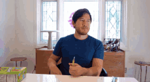 a man in a blue shirt sits at a table with a box of skittles