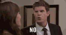 a man in a suit and tie is talking to a woman and saying `` no '' .