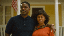 a man and a woman are posing for a picture in front of a house with hbo written on the bottom