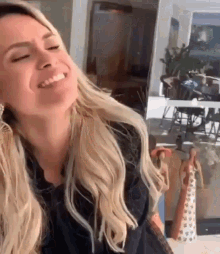 a woman with blonde hair is laughing with her eyes closed .