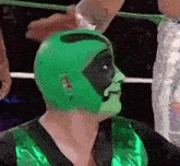 a wrestler wearing a green mask and a green vest is being held by another wrestler .