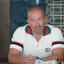a bald man wearing a white polo shirt with a gucci logo