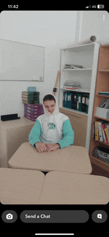 a phone screen shows a person sitting at a desk and says send a chat at the bottom