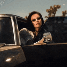 a woman wearing sunglasses is sitting in a car and looking out the window .
