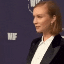 a woman in a tuxedo and white shirt is standing in front of a sign that says wif