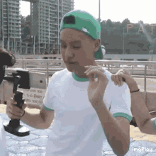 a man wearing a green hat and white shirt is holding a cell phone