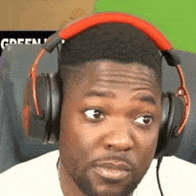 a man wearing headphones looks at the camera with a green background behind him