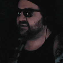 a man with a beard wearing sunglasses and a black tank top .
