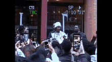 a group of people are taking pictures of a man in front of a store with a sign that says tbc