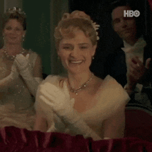 a woman in a white dress and gloves is smiling and clapping .