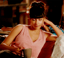 a woman in a pink tank top sits on a couch holding a coffee mug