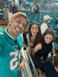 a man wearing a miami dolphins jersey laughs with two women