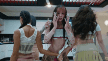 a group of women are standing in a kitchen and one of them is wearing a crop top with polka dots on it