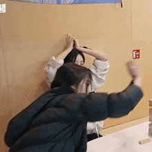 two women are playing a game with a red fire extinguisher on the wall behind them