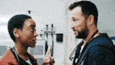 a man and a woman are standing next to each other in a hospital room and talking to each other .
