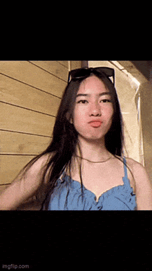 a young woman wearing sunglasses and a blue dress makes a funny face