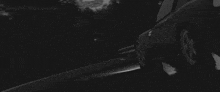 a black and white photo of a car driving down a road at night .