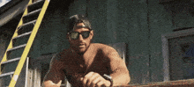 a shirtless man wearing sunglasses and a hat is standing in front of a ladder