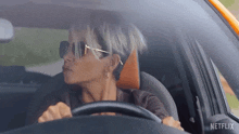 a woman wearing sunglasses is driving a car with netflix written on the side