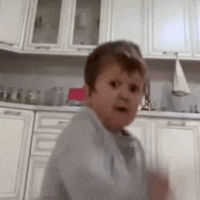 a young boy is making a funny face in a kitchen with white cabinets .