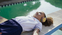 a girl wearing headphones is laying on a ledge by a pool