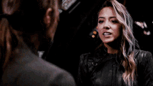 a woman in a leather jacket is standing next to a man in a suit and talking to him .