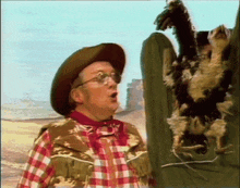 a man in a cowboy hat and plaid shirt is holding a dead bird