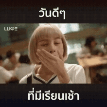a girl with blonde hair is covering her mouth with her hand .