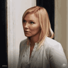 a woman in a white suit and a white shirt is standing in a doorway .