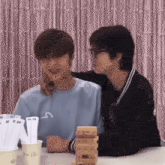 two young men are sitting at a table playing a game .