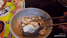 a person is holding chopsticks over a bowl of food with the words made in animotica on the bottom right