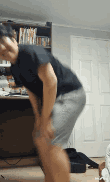 a man in a black shirt and grey shorts is standing in front of a bookshelf