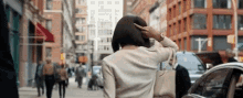 a woman is walking down a busy city street while holding her hair .