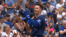 a baseball player is holding his helmet in the air in front of a crowd of people .