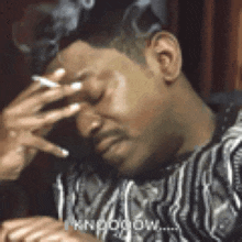 a man is smoking a cigarette and rubbing his forehead .