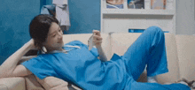 a woman in scrubs is laying on a couch looking at her cell phone .