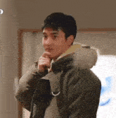 a young man in a parka with a fur hood is standing in a room .