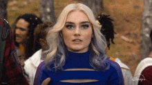 a woman with blonde hair and purple highlights is wearing a blue sweater with a cut out in the front