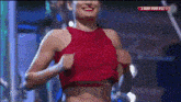 a woman in a red crop top is smiling while holding her breasts